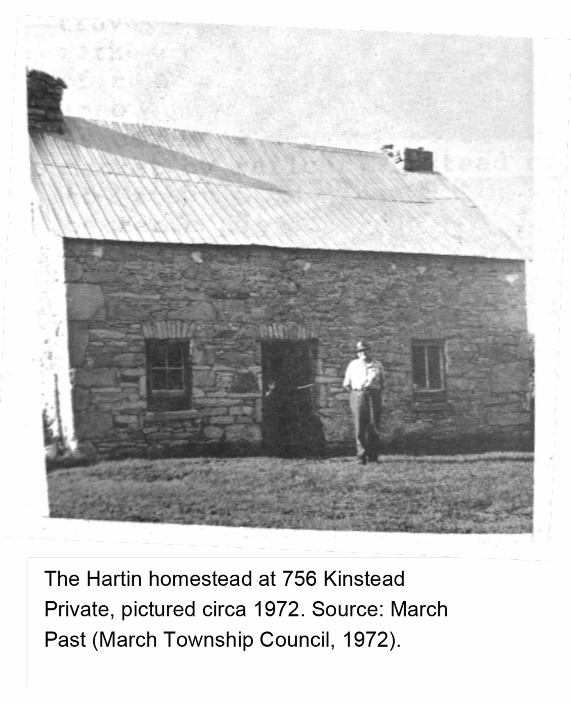 Black-and-white photograph of the Hartin homestead at 756 Kinstead Private, a one-and-a-half-storey stone farmhouse with a metal roof and two chimneys. A person stands near the central doorway on the grass in front of the building. The image dates from approximately 1972.